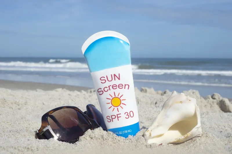 Sun screen bottle and sunglasses on a sandy beach - 10 Simple Sunburn Hacks to Soothe Your Skin