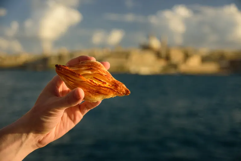 Traditional savoury pastry Pastizzi from Malta with ricotta filling. Valletta on background